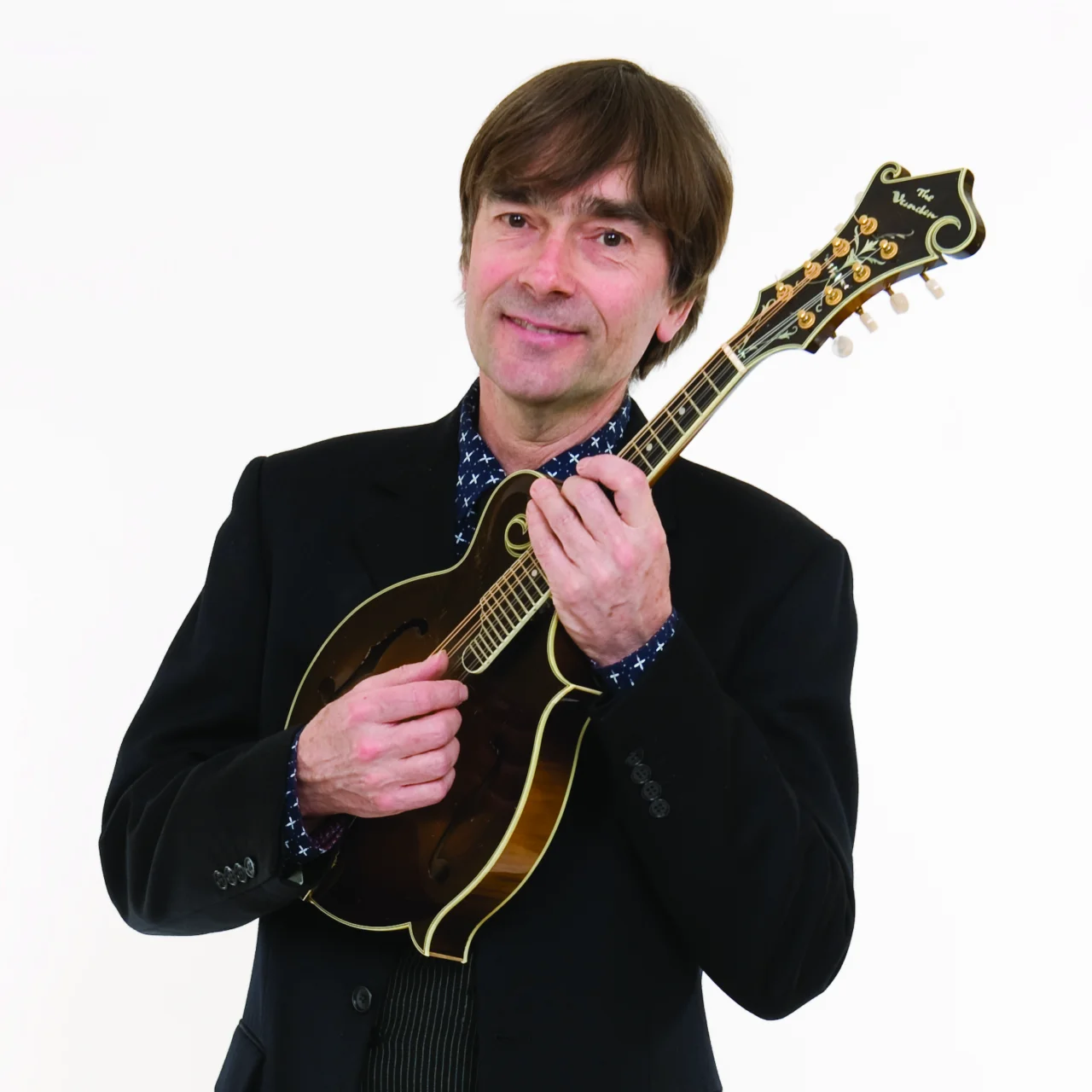 Simon is smartly dressed in a suit and looks into the camera with a smile. He is playing a mandolin.