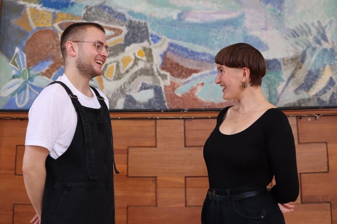 Sophie Crawford and George Sansome share a giggle together whilst standing in front of an abstract and colourful mural.