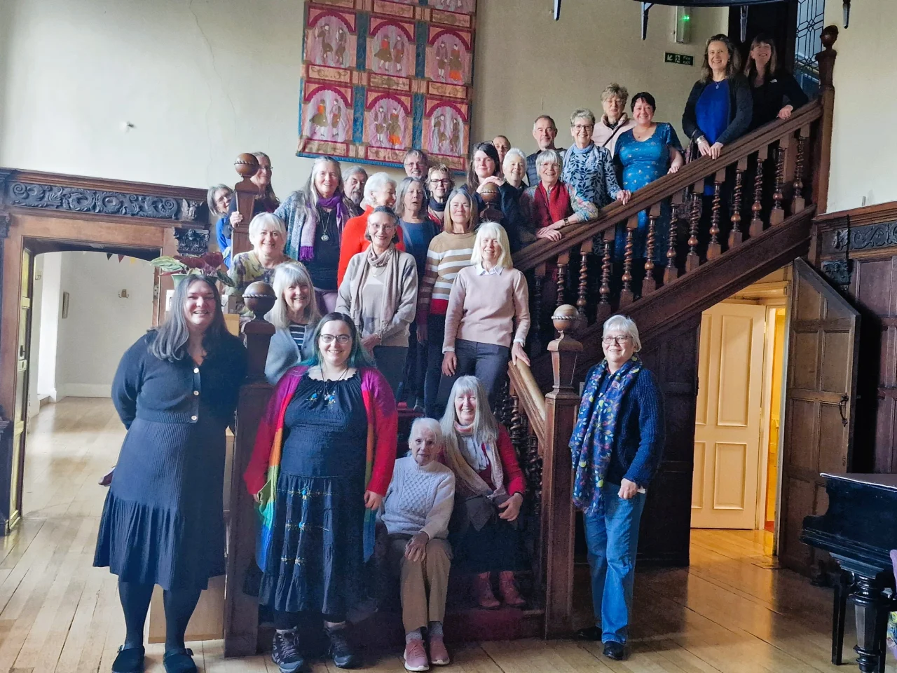 A group of men and women stand on the staircase at Halsway Manor.